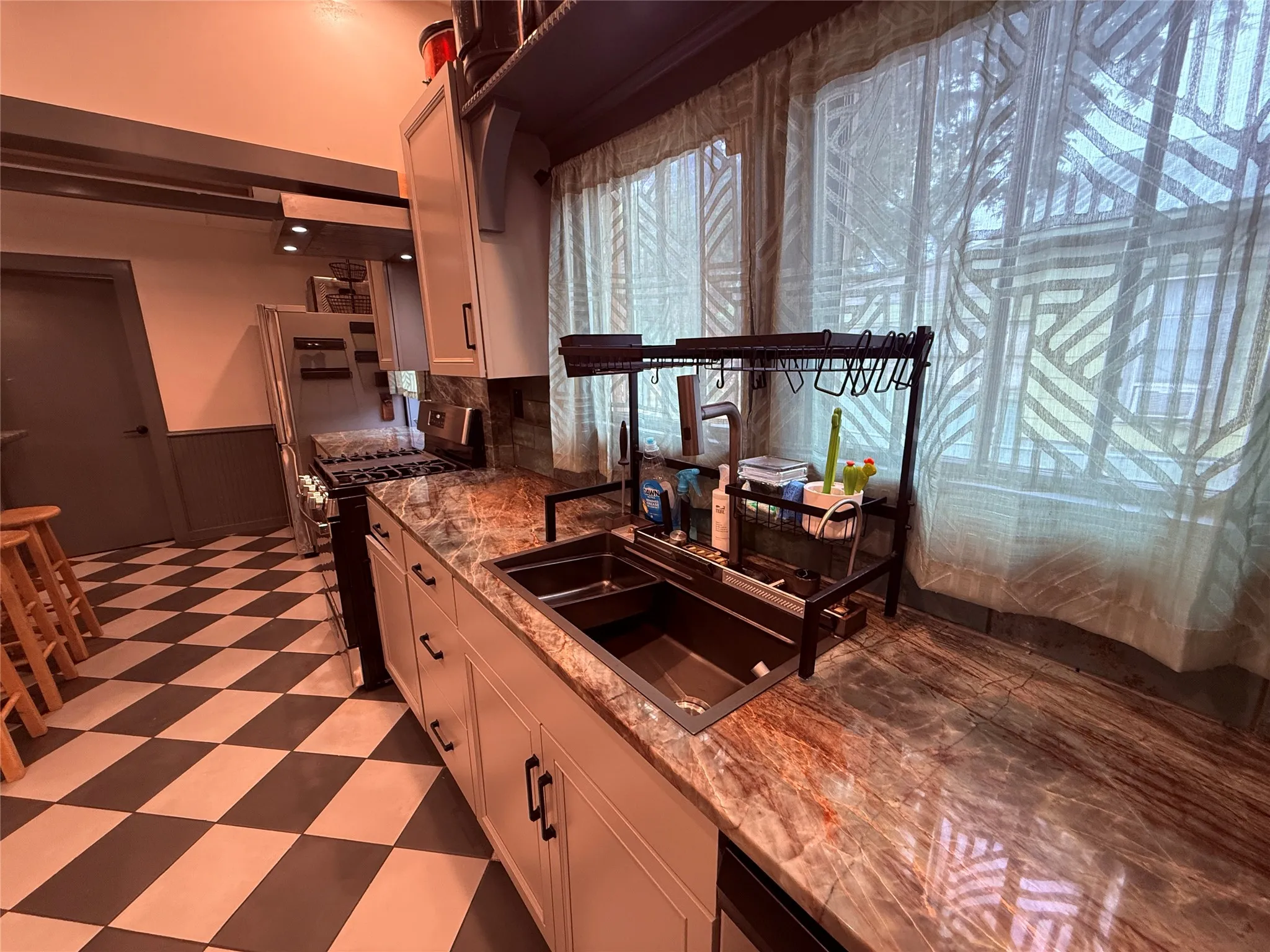 Kitchen featuring checkered floor tiling, stainless steel appliances, light-toned cabinetry, and extensive counter space with a built-in sink