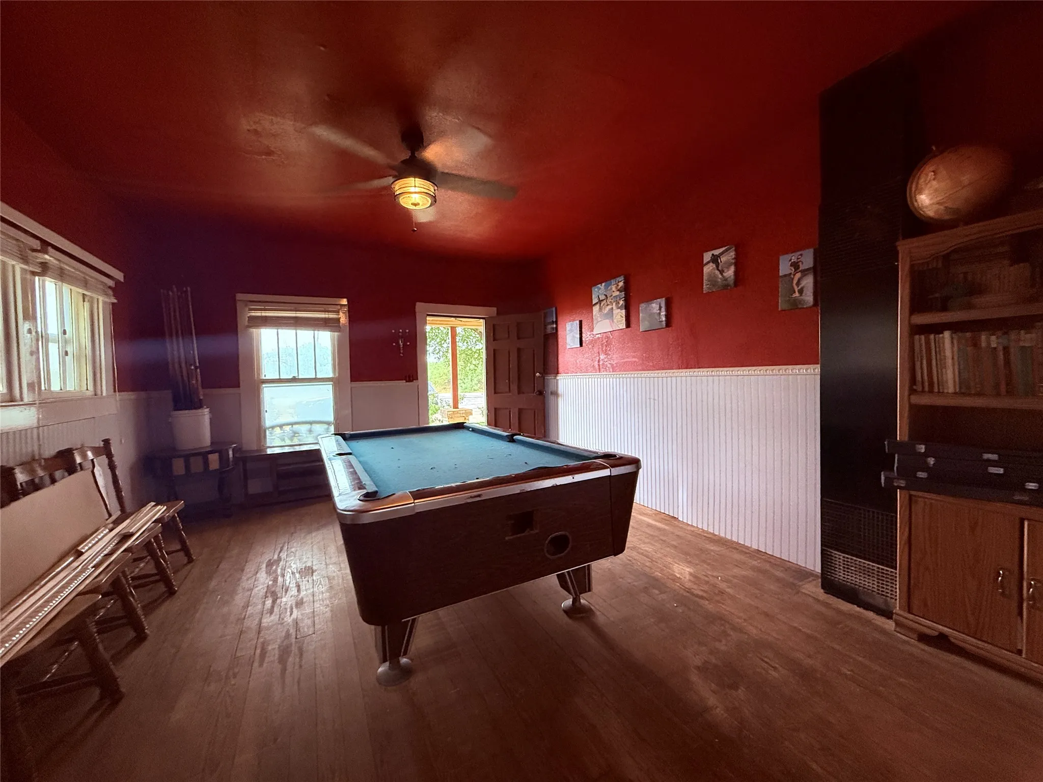 Wood-finish flooring, paneled wainscoting, ceiling fan with integrated lighting, and multiple windows
