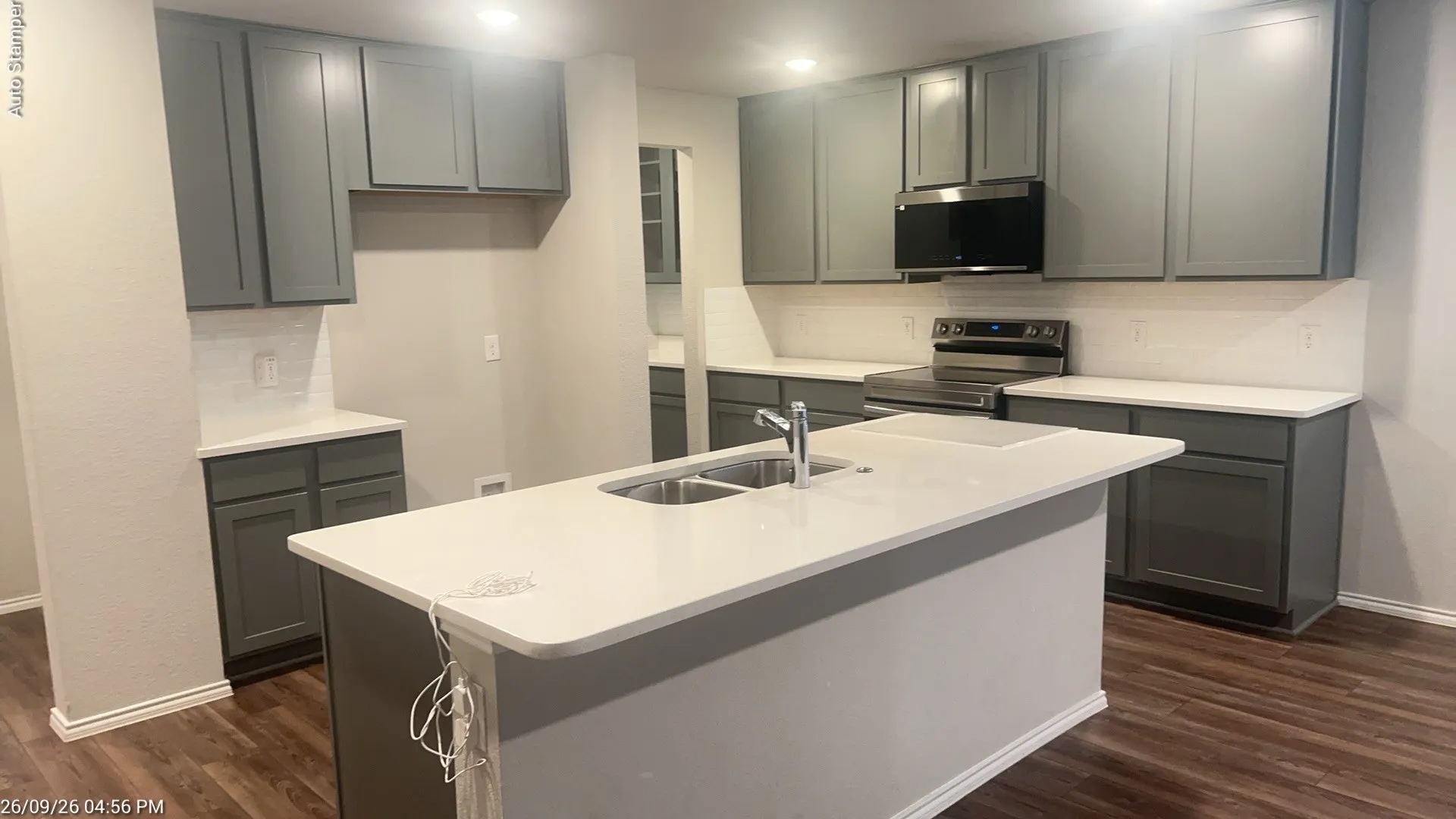 Spacious kitchen featuring an island with an integrated sink, grey cabinetry, light-toned countertops, a subway tile backsplash, and wood-finish flooring