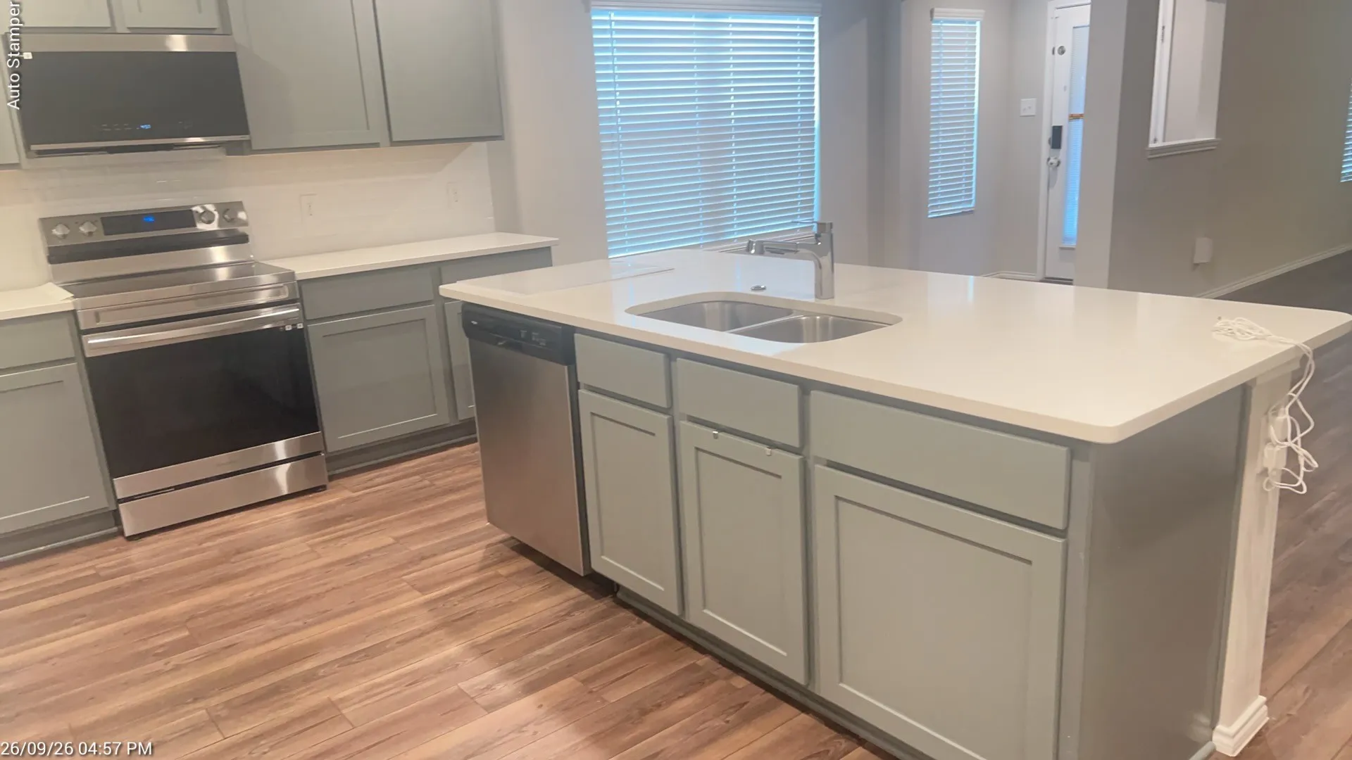 Kitchen featuring wood-finish flooring, light grey cabinetry, stainless steel appliances, and a central island with a double basin sink and light-toned countertop