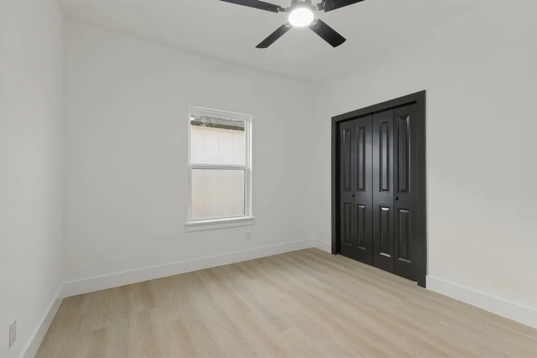 Light wood-finish flooring, white walls, and a ceiling fan with integrated lighting