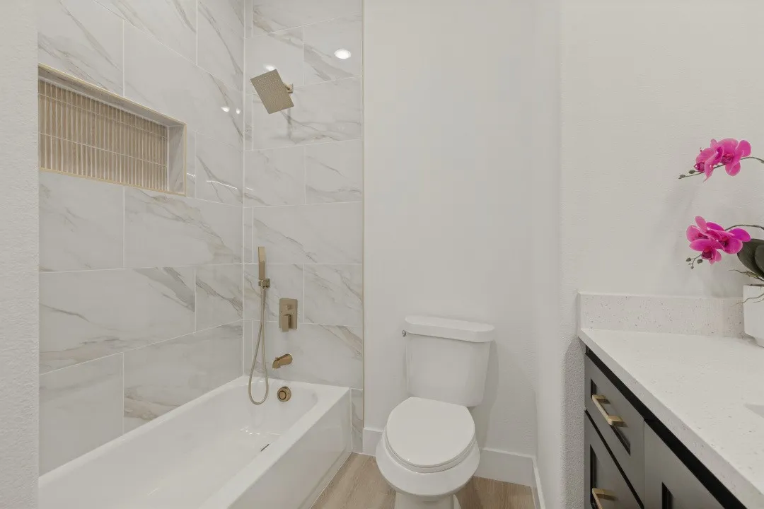 Bathtub with large format wall tiling, recessed shower niche, and gold-finish fixtures