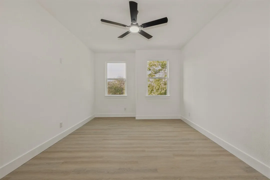 Light-filled room featuring two windows, wood-finish flooring, a ceiling fan with integrated lighting, and white walls