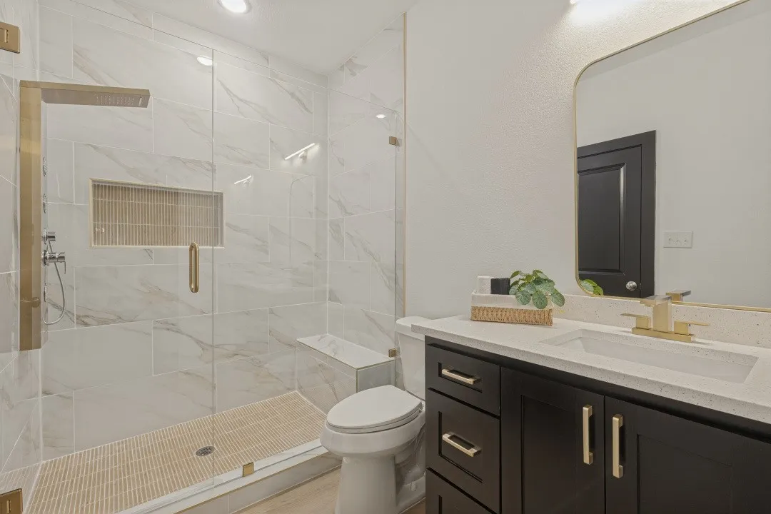 Glass-enclosed shower with a built-in bench, recessed shelf, and gold-finish fixtures