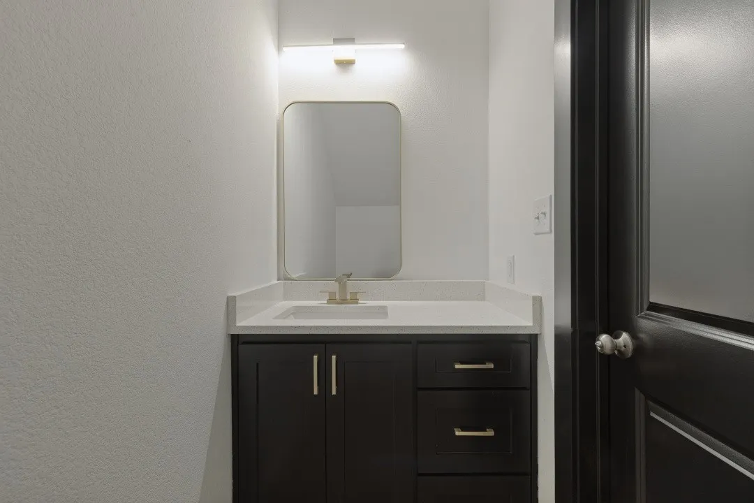 Dark wood-finish vanity with gold-tone hardware, white countertop, rectangular undermount sink, and wall-mounted gold-tone faucet