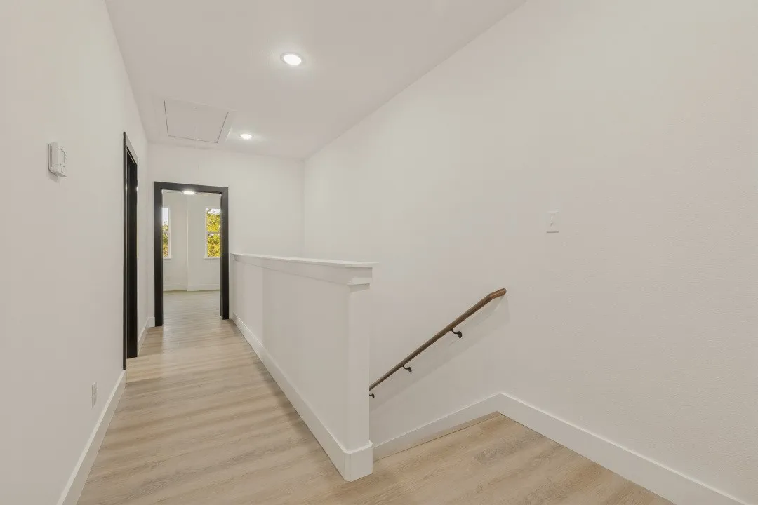 Light wood-finish flooring, recessed ceiling lighting, a white painted railing, and dark trim doorways