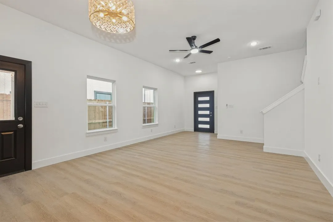 Wood-finish flooring throughout, white walls, black ceiling fan, recessed lighting, and a contemporary front door with horizontal glass inserts