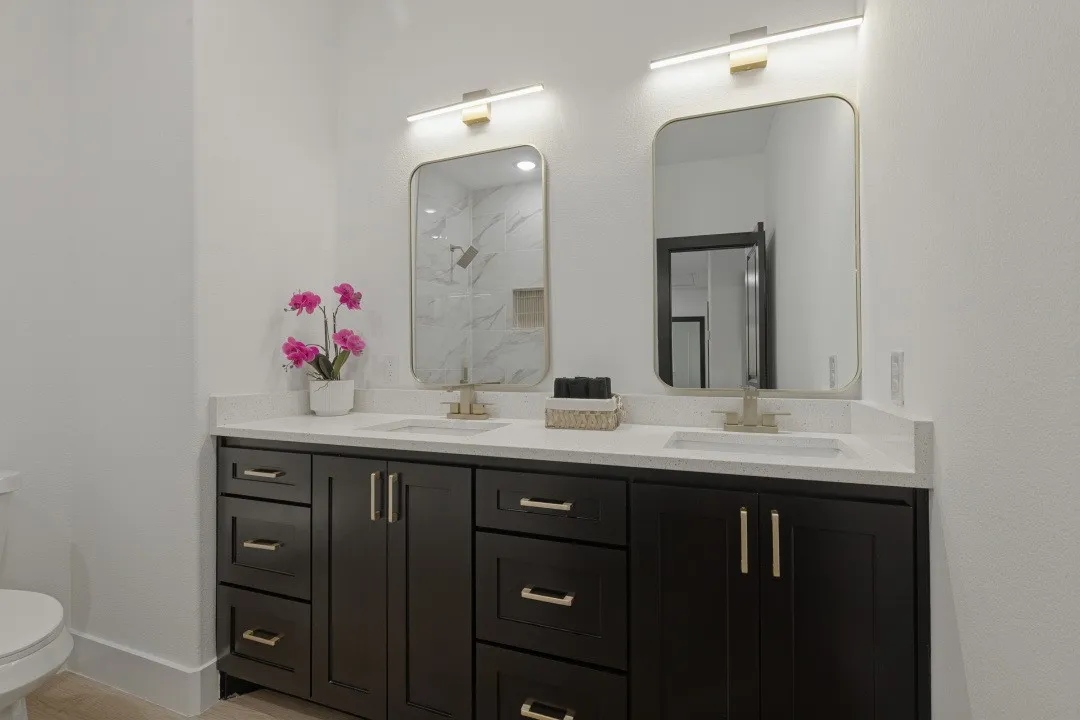 Dual vanity with dark wood cabinetry, white countertops, undermount sinks, and gold-finish hardware