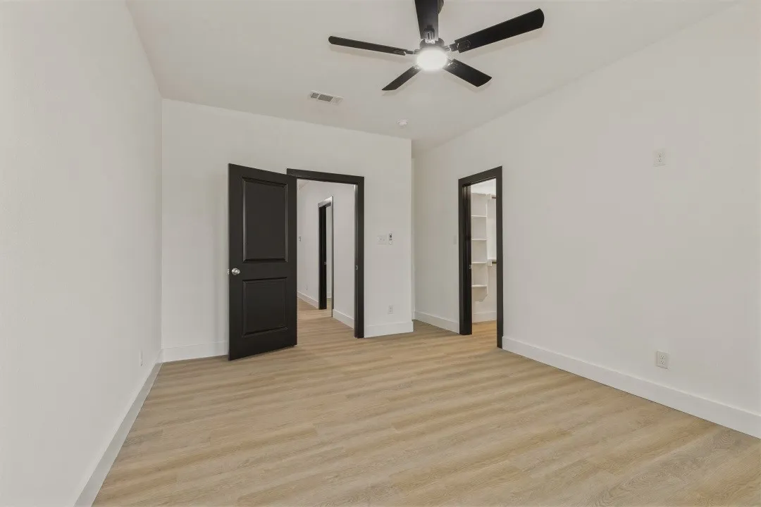 Spacious room with wood-finish flooring, crisp white walls, a contemporary ceiling fan, and dark-paneled doors