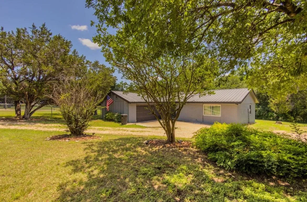 House with a metal roof, attached garage, and surrounding mature trees and landscaping