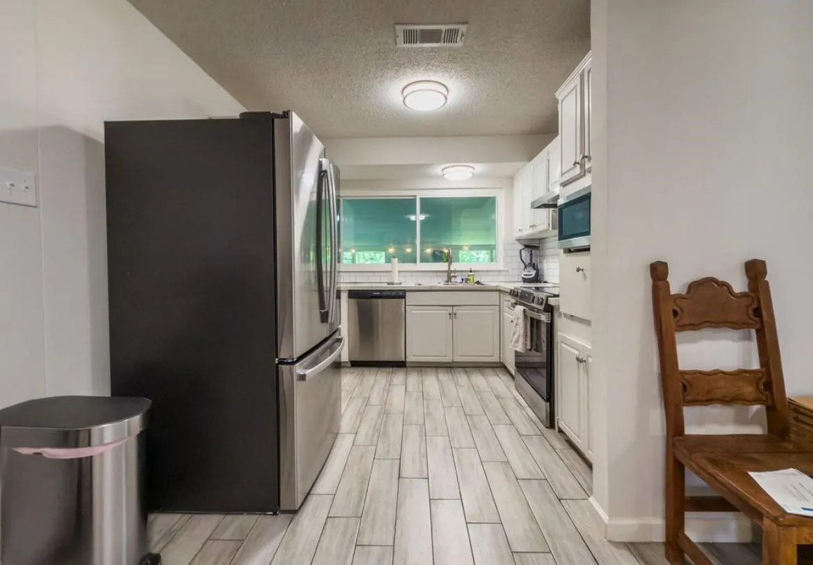 Kitchen featuring wood-finish flooring, white cabinetry, a subway tile backsplash, and stainless steel appliances