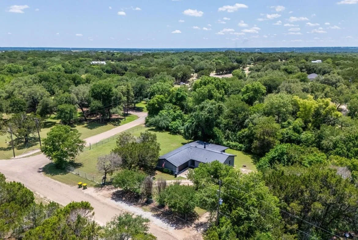 Extensive natural landscaping with mature trees, gravel driveways, and a fenced perimeter