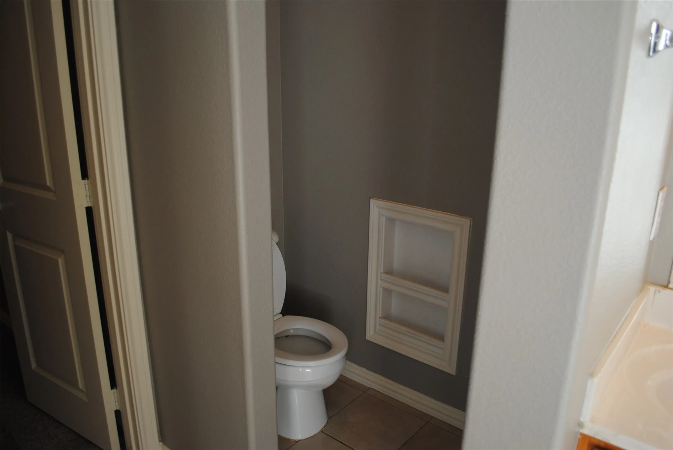 Recessed wall shelving, tiled flooring, and a white toilet