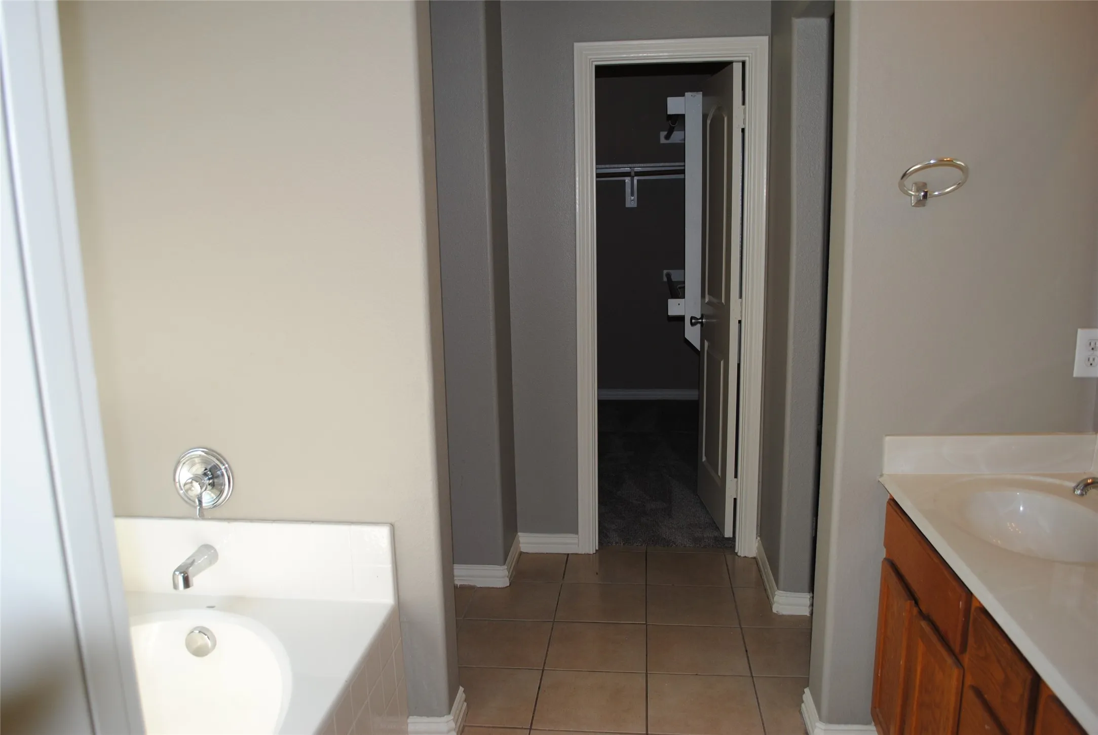 Bathroom featuring a built-in bathtub with chrome fixtures, a vanity with wood-finish cabinetry, a white countertop with an integrated sink, and tile flooring