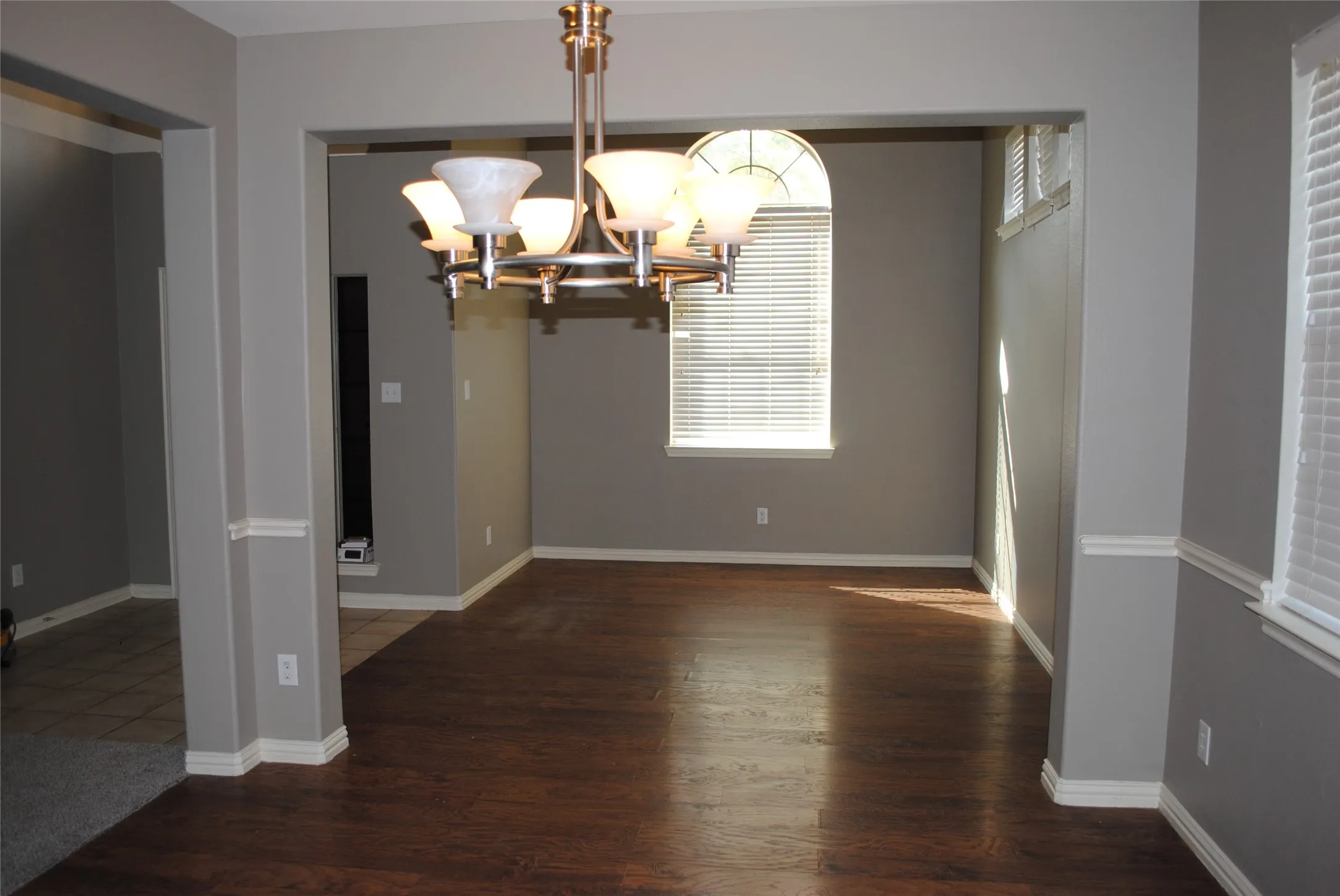 Wood-finish flooring, arched window with horizontal blinds, decorative ceiling light fixture, neutral wall color, and white trim