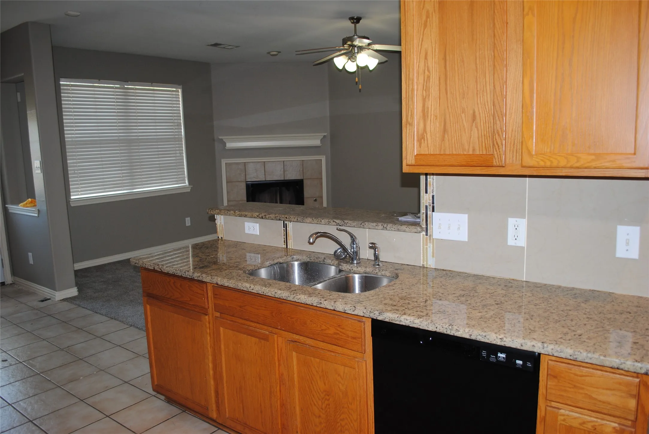 Granite countertops, double basin sink, wood cabinetry, black dishwasher, and tile flooring