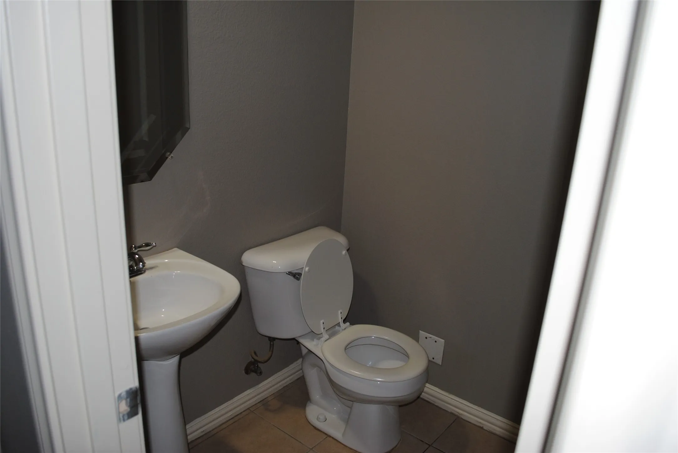 Downstairs half bath. Pedestal sink with chrome fixtures, white toilet, and tile flooring