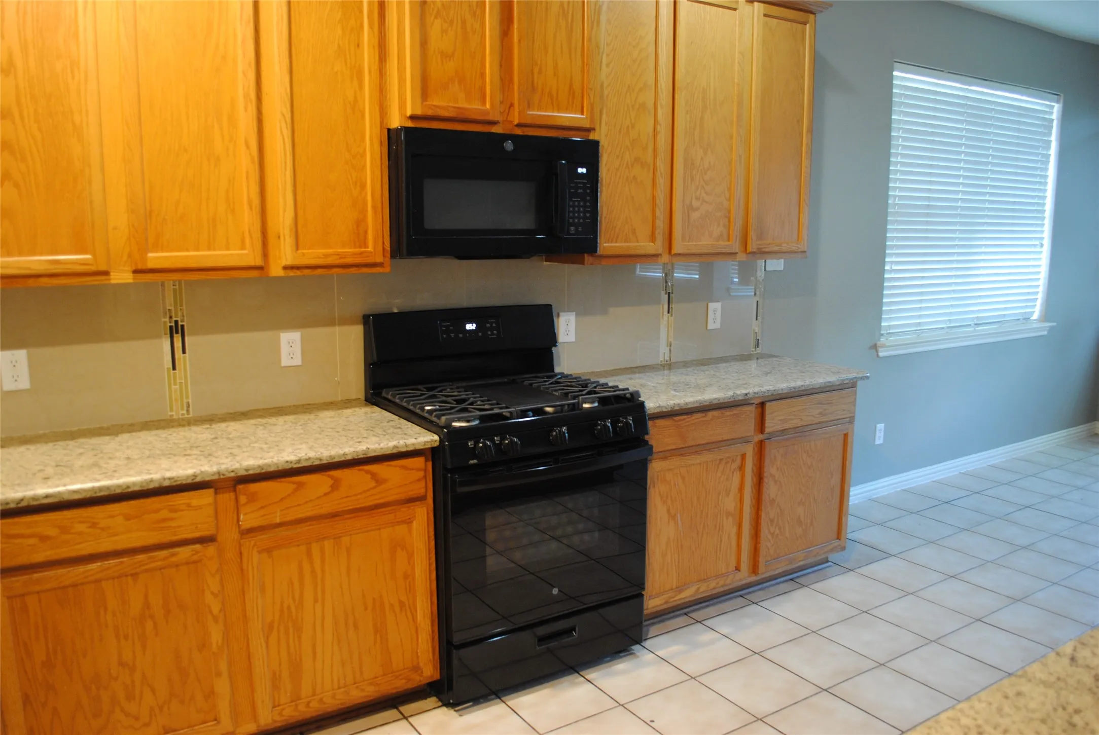 Kitchen featuring light wood cabinetry, stone countertops, black gas range, built-in microwave, and tile flooring