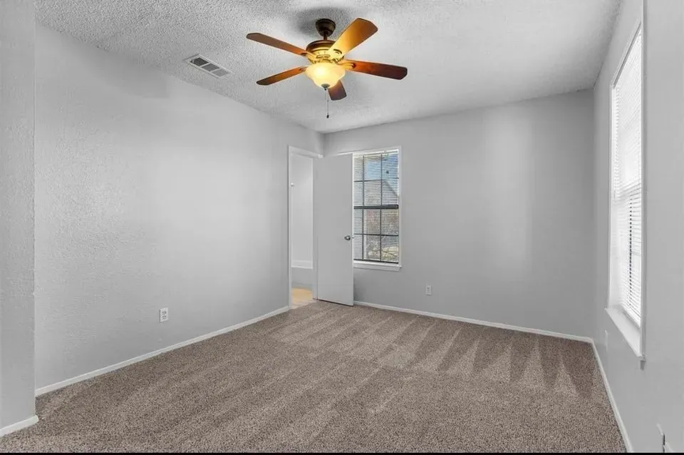 A cozy bedroom featuring a neutral-colored carpet, ceiling fan and tall windows, creating a comfortable atmosphere.