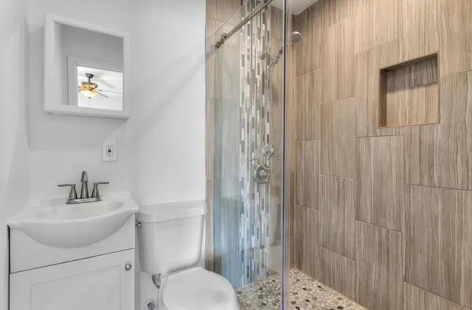 Bright bathroom showcasing a shower stall, toilet and vanity with mirror, designed with neutral-colored walls.
