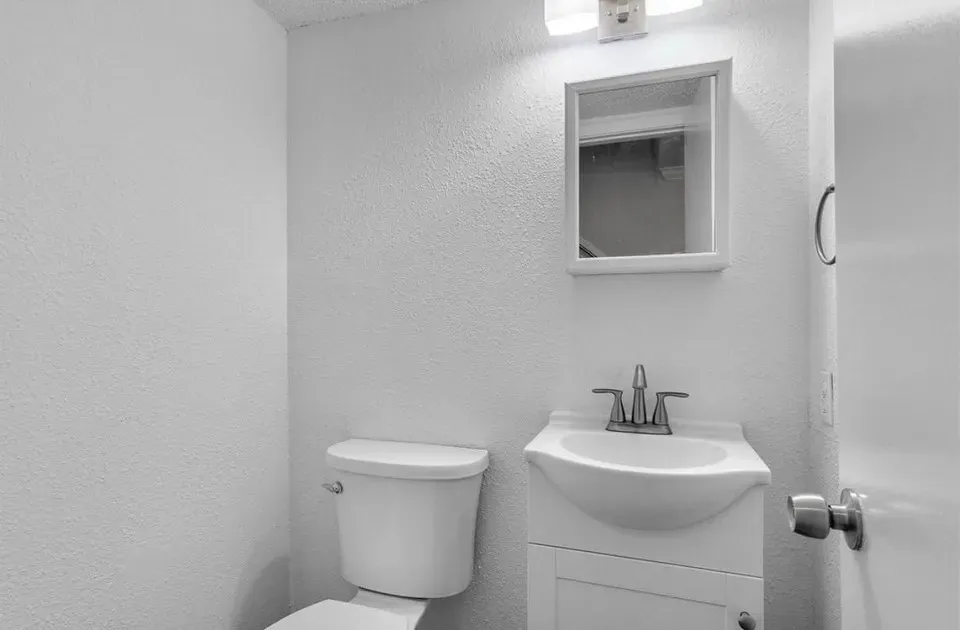 A bright white half bathroom showcasing a toilet, a modern vanity with a simple mirror on the wall.