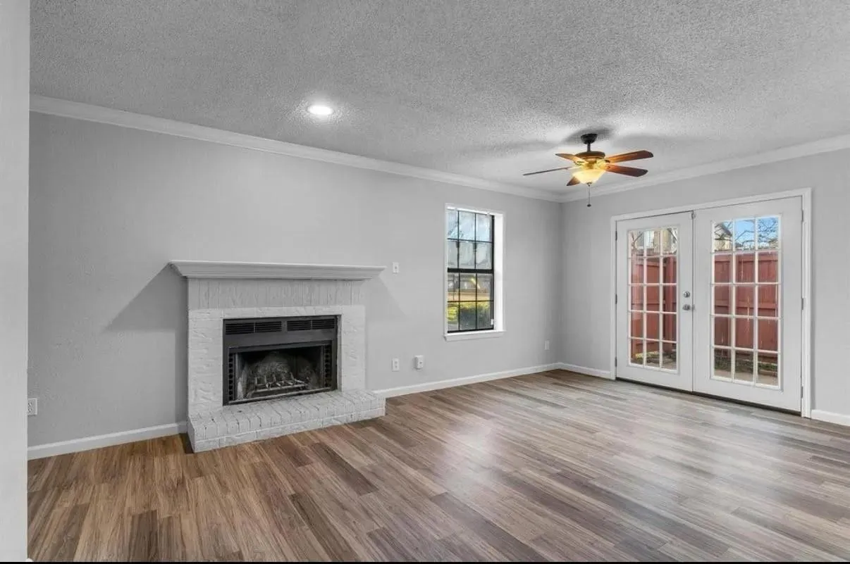 A spacious living room featuring a ceiling fan, a fireplace and a glass door, creating a cozy yet open atmosphere.