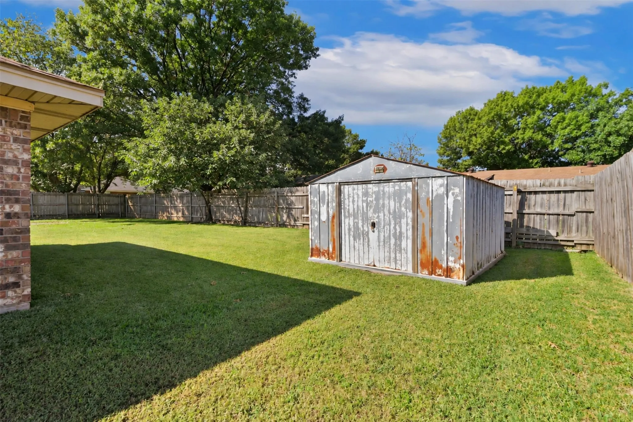 Expansive grassy yard with a storage shed and a wood-panel fence