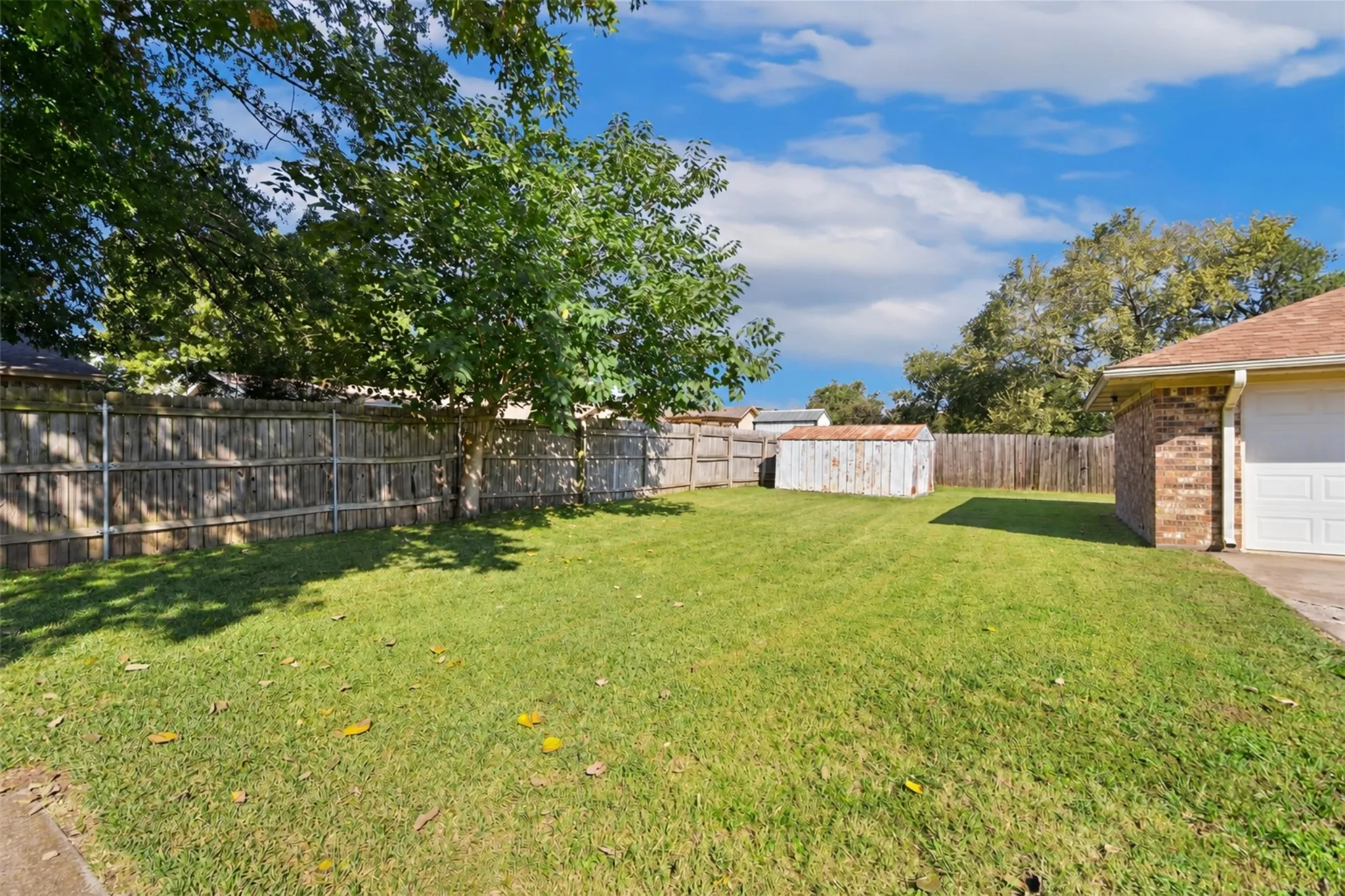 Manicured lawn with mature trees, wood fence enclosure, and brick exterior construction
