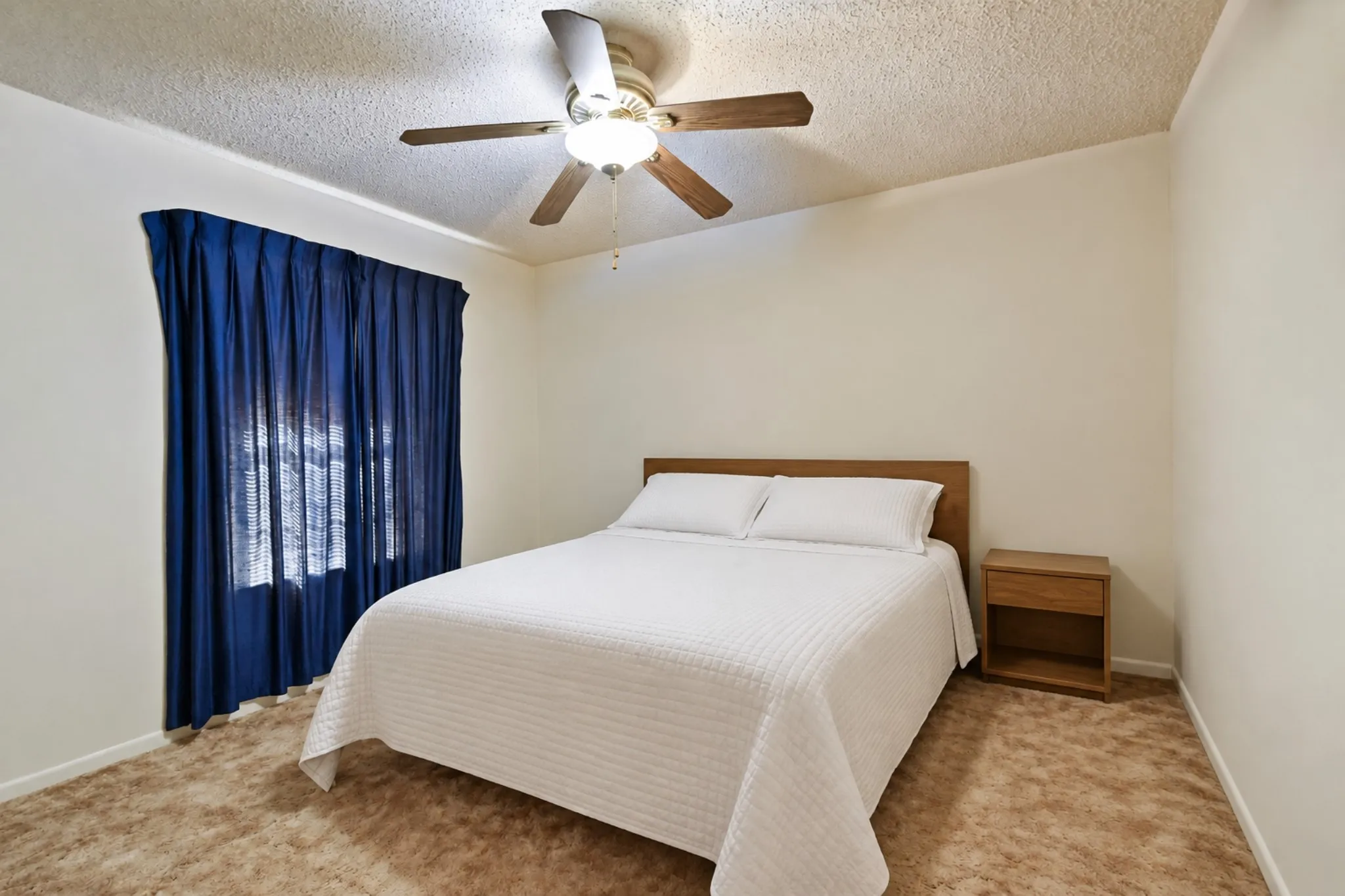 Neutral wall tones, ceiling-mounted fan with integrated lighting, and a window with privacy coverings