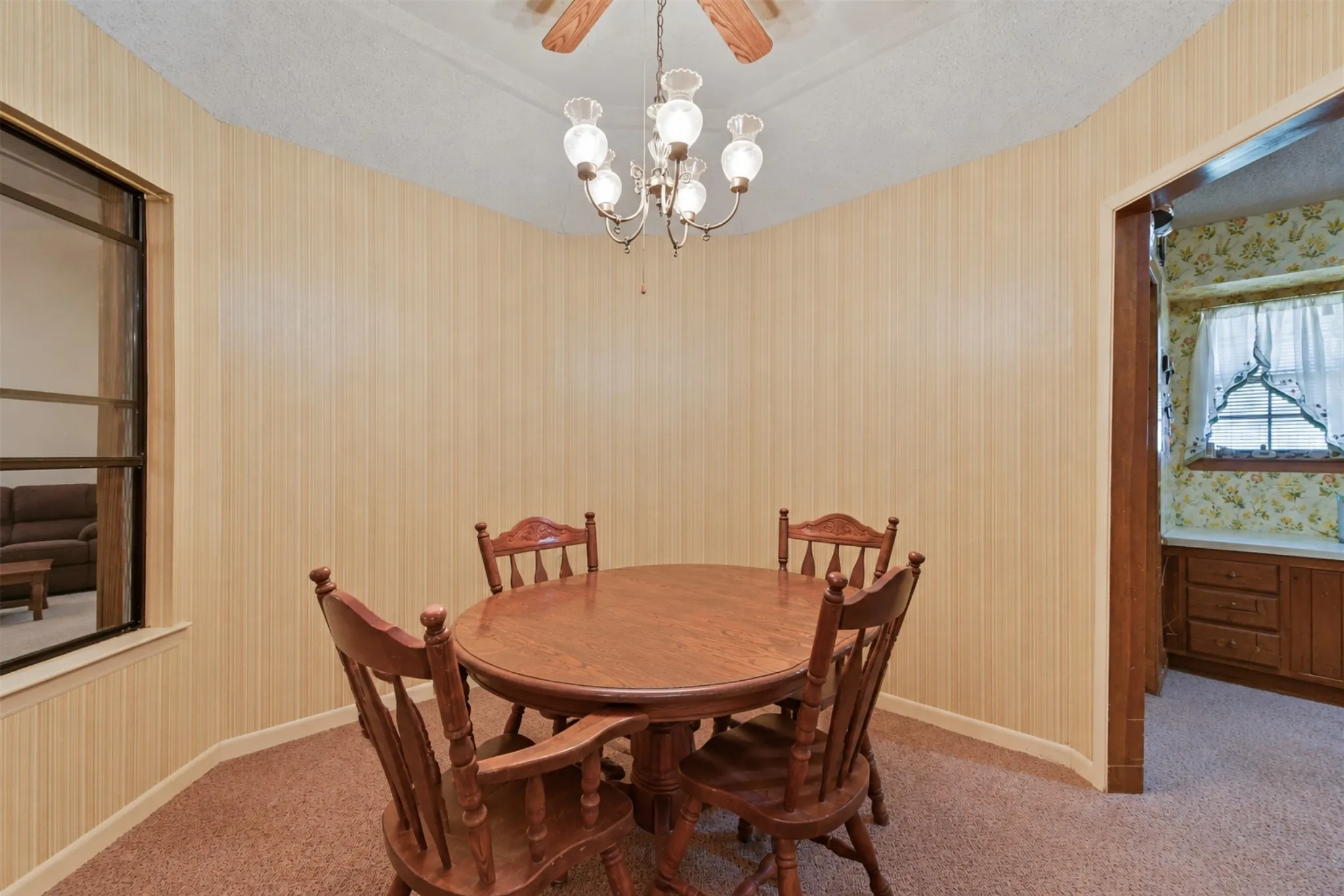 Textured wall paneling with a classic chandelier, ceiling fan, and carpeted flooring