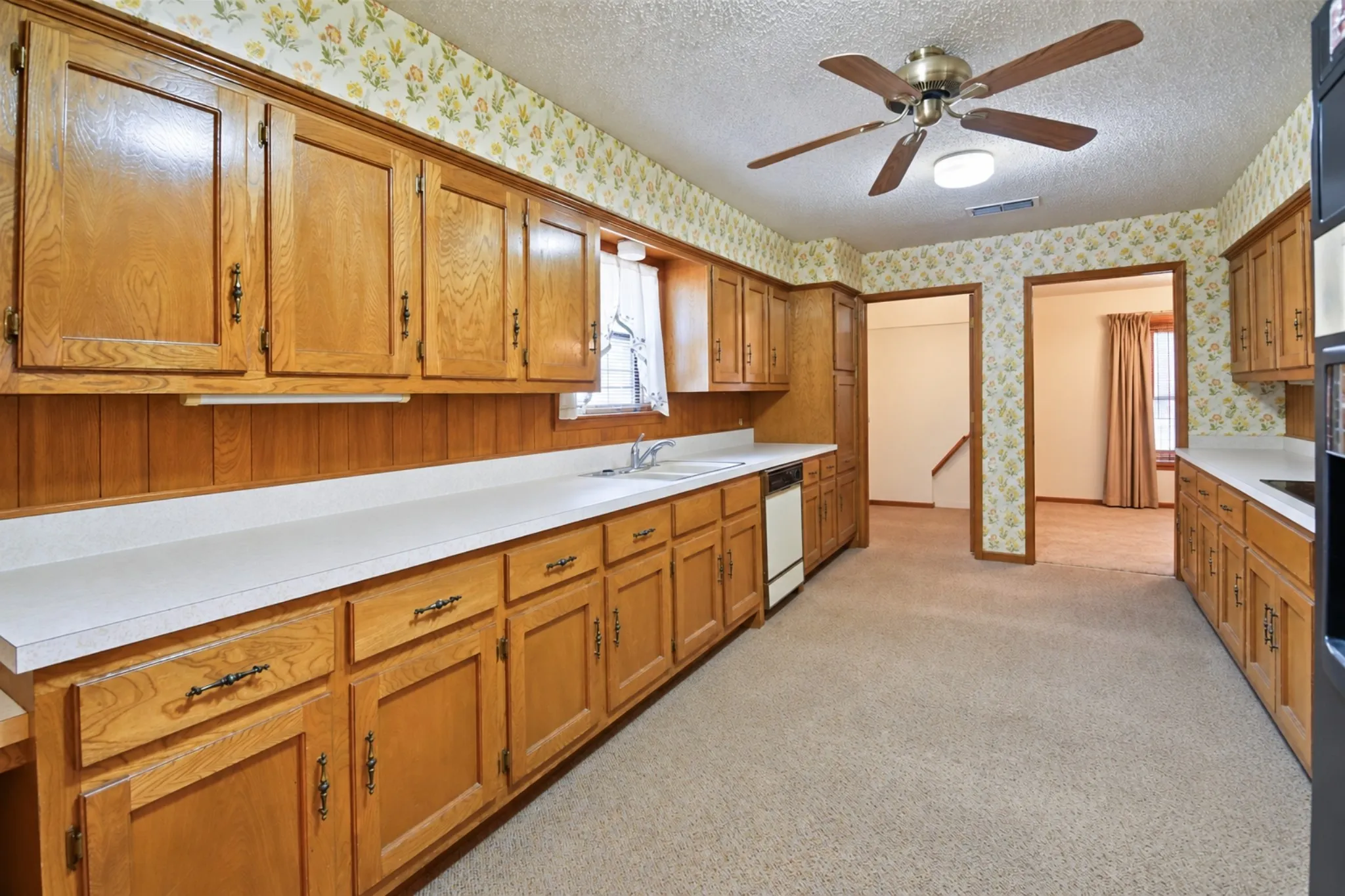 Kitchen featuring wood cabinetry, white countertops, built-in dishwasher, and carpet flooring