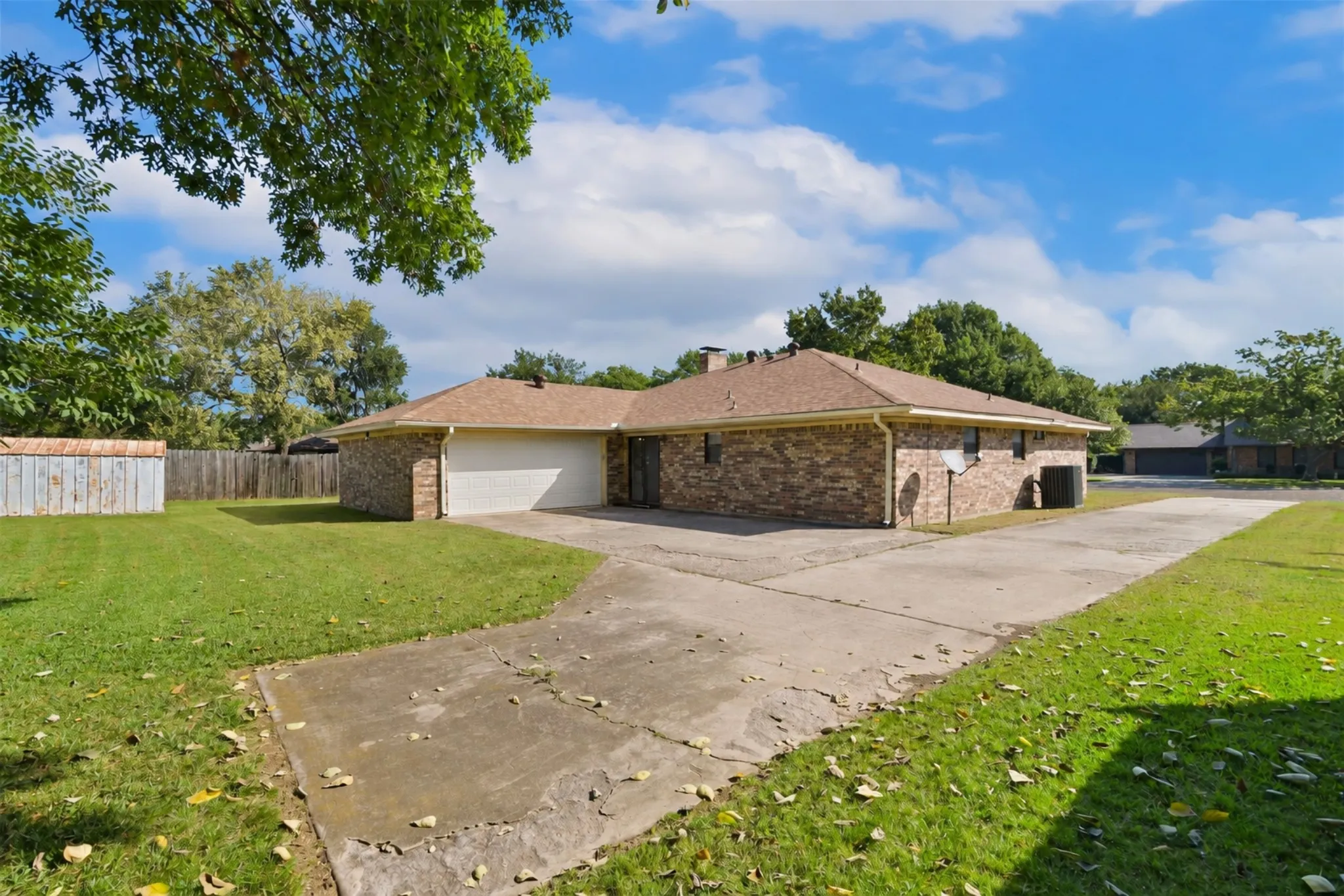 Brick exterior with an attached garage, paved driveway, and a spacious green lawn