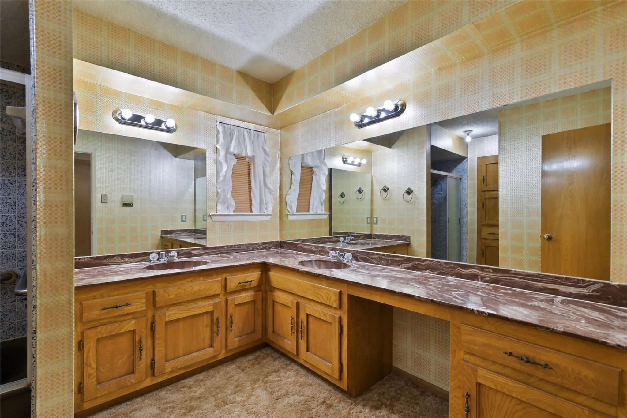 Dual vanity with integrated sinks, expansive wall-mounted mirror, wood-finish cabinetry, and sconce lighting