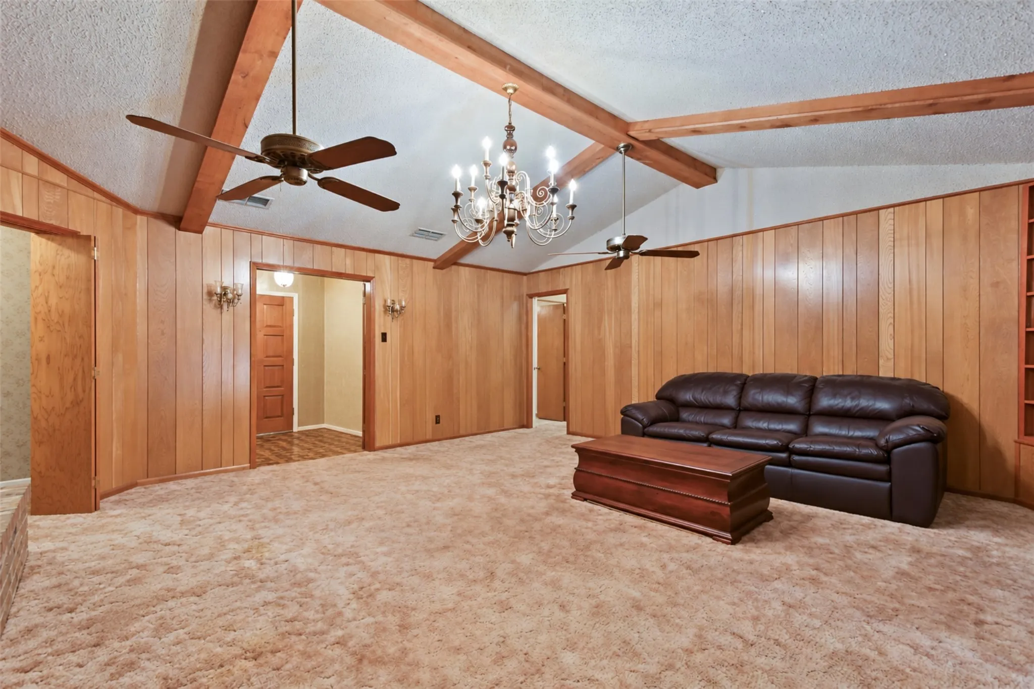 Vaulted ceiling with exposed wood beams, wood paneling, dual ceiling fans, and a chandelier