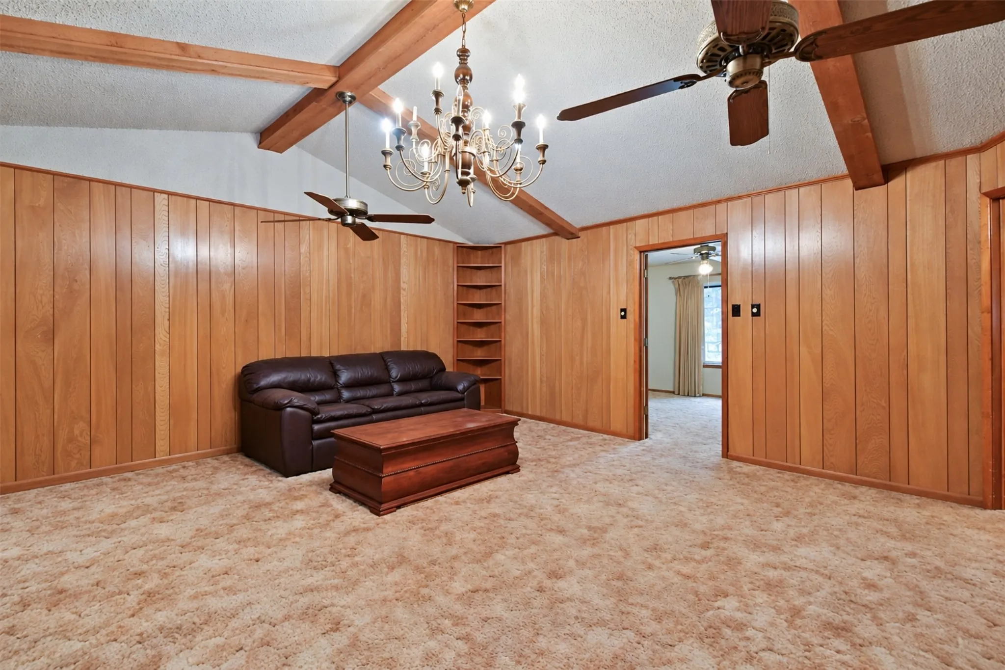 Vaulted ceiling with exposed wood beams, wood paneling, built-in shelving, and two ceiling fans with integrated lighting
