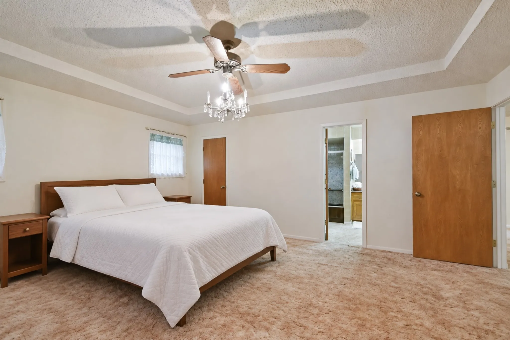 Recessed tray ceiling with a ceiling fan, a chandelier light fixture, and wood doors