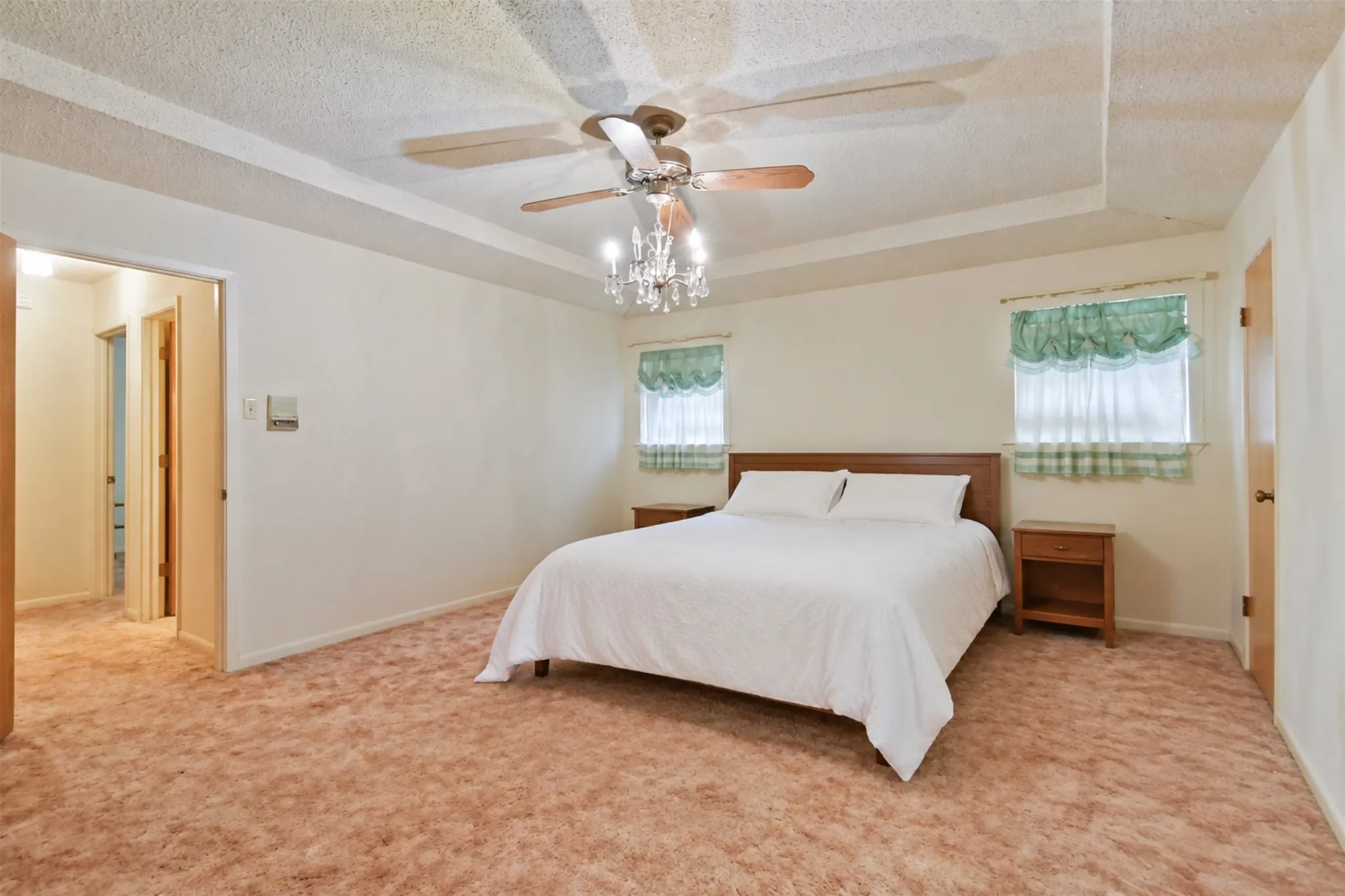 Tray ceiling with a decorative chandelier and a ceiling fan, dual windows, and wall-to-wall carpeting