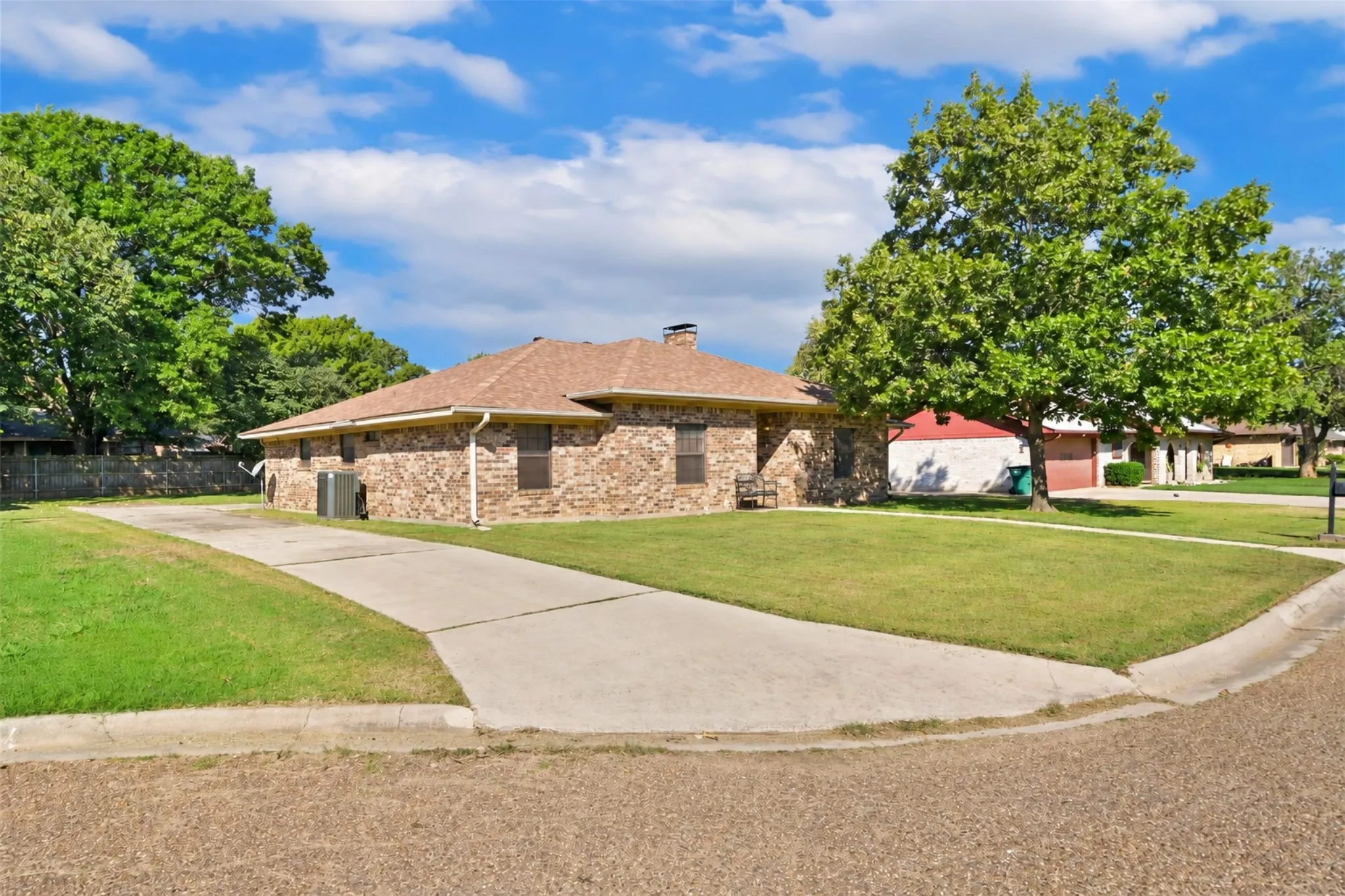 Brick exterior with a shingle roof, concrete driveway, and mature trees