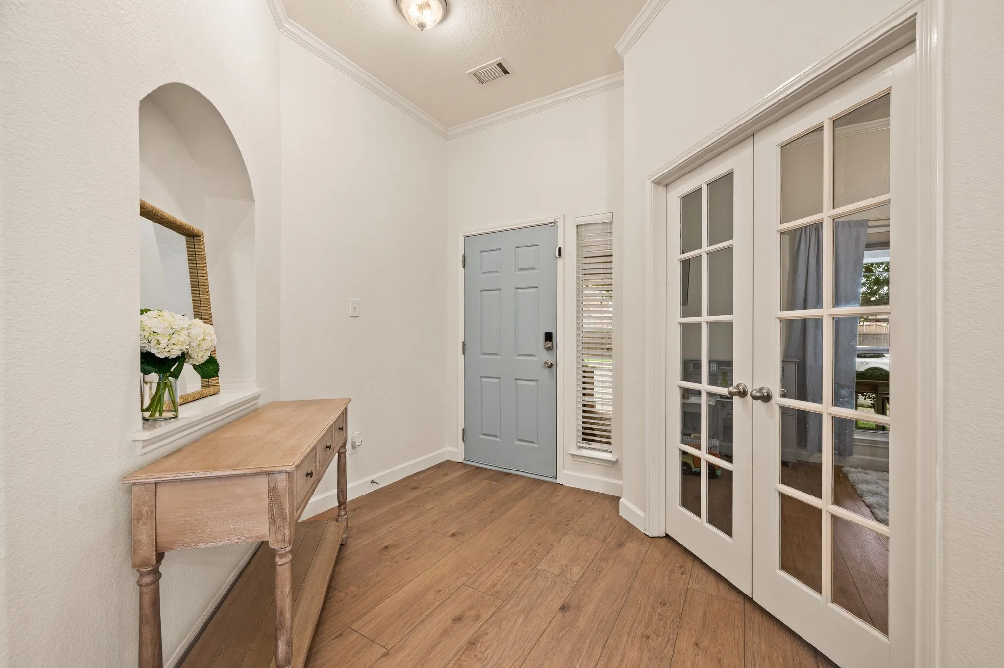 Light wood-finish flooring, white walls, arched wall niche, French doors with glass panes, and a contemporary ceiling light fixture
