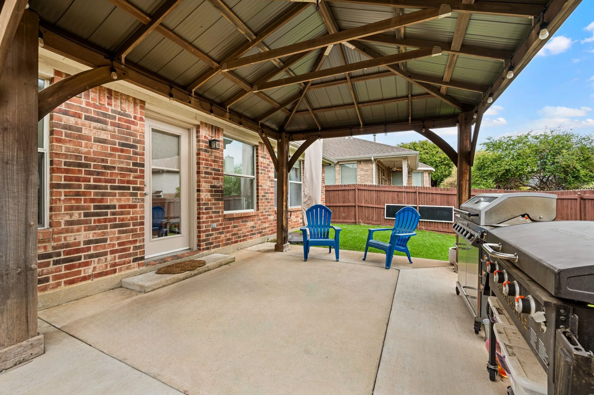 Expansive concrete patio with a permanent gazebo structure, brick exterior, and a fenced backyard
