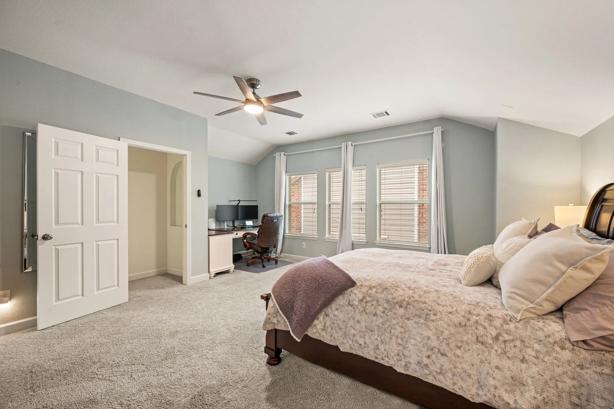 Vaulted ceiling with a ceiling fan, three paneled windows with blinds, light gray wall paint, and gray carpet flooring