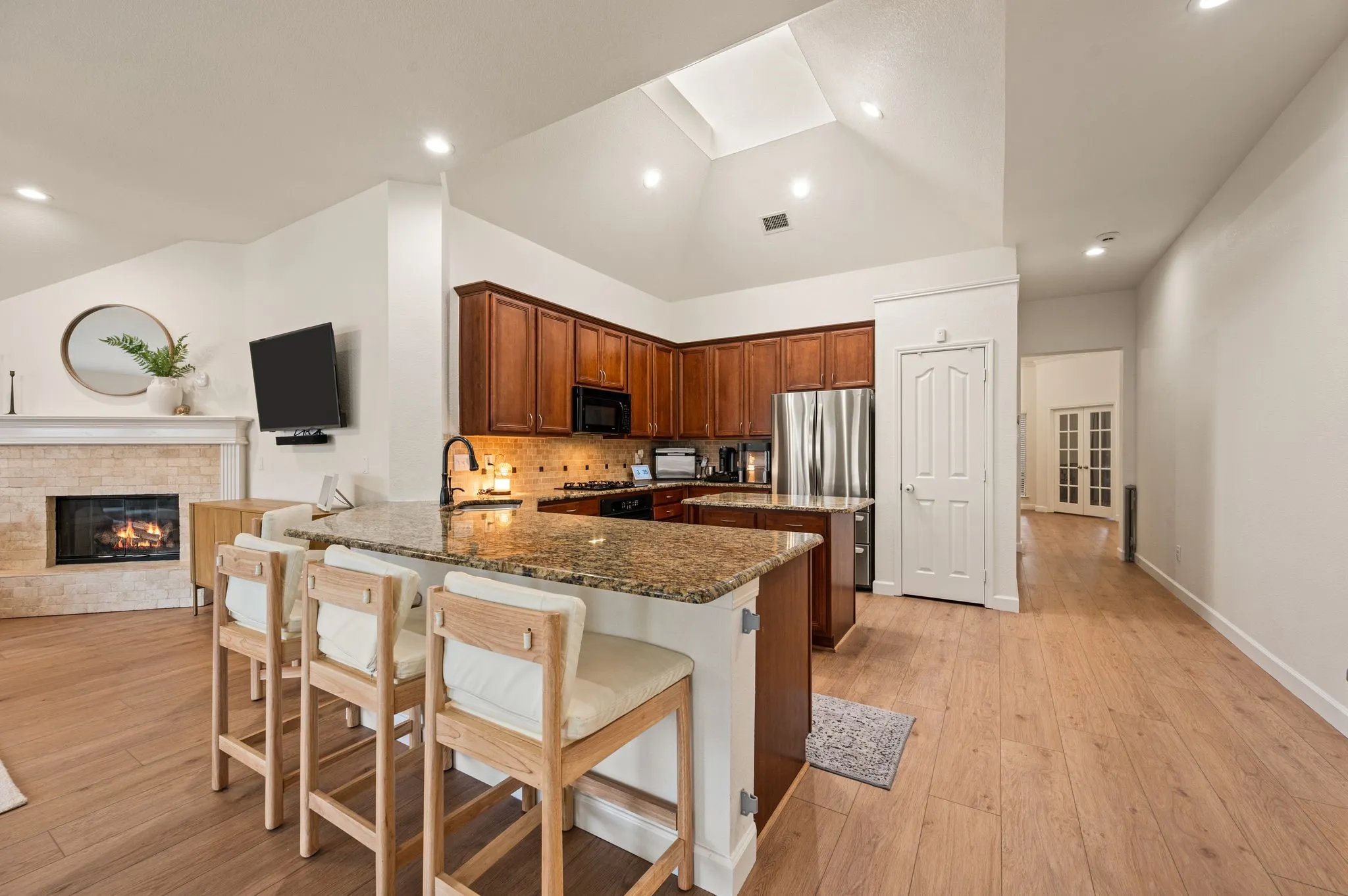Wood-finish flooring, vaulted ceiling, skylight, kitchen island with built-in cabinetry, and stone-tiled fireplace