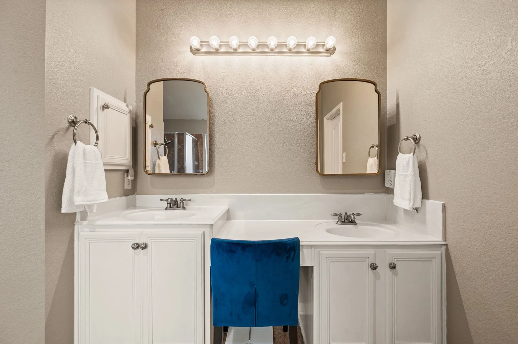 Dual vanities with integrated sinks, white cabinetry, individual framed mirrors, and a dedicated vanity space