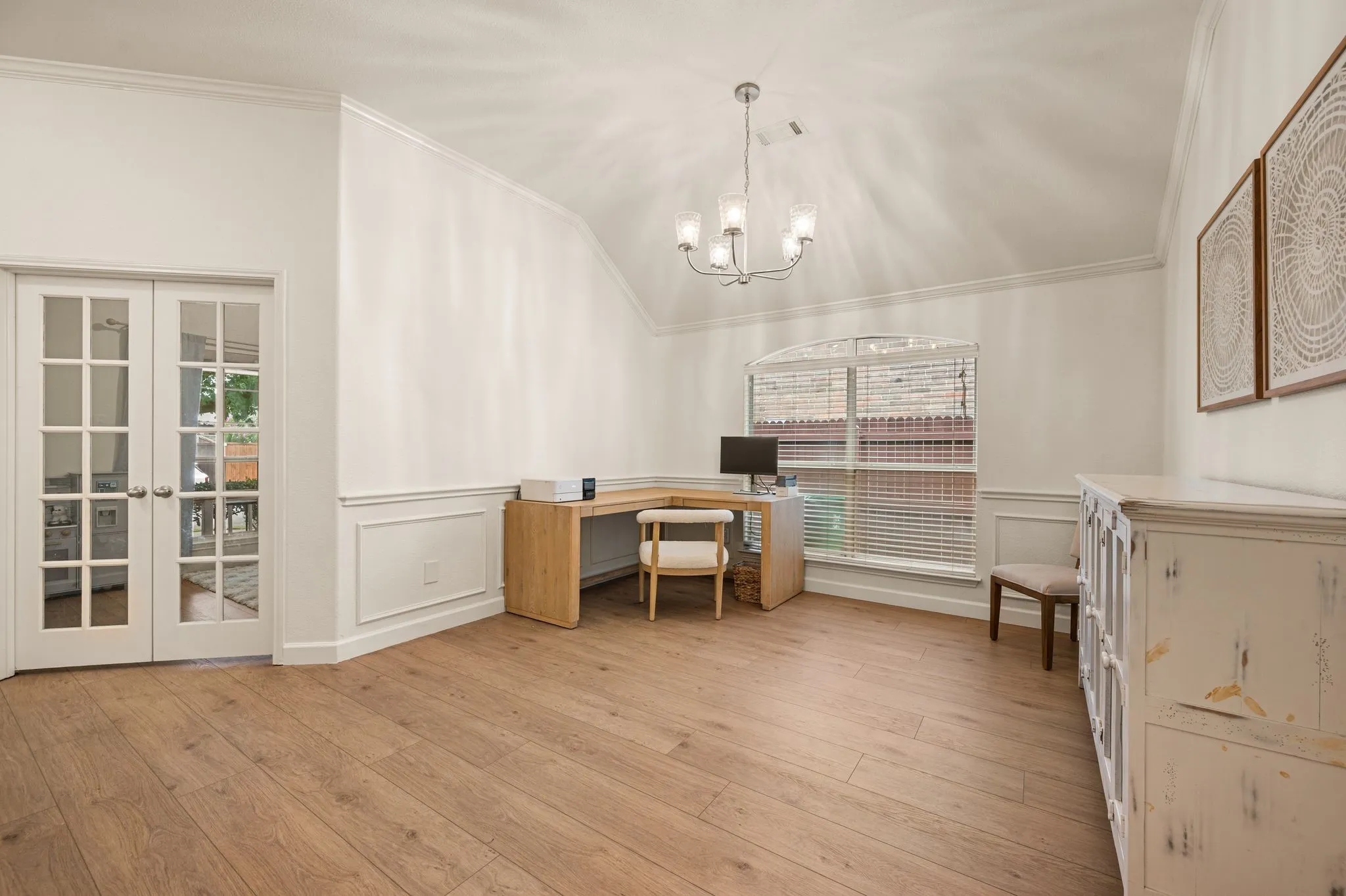 Vaulted ceiling, wood-finish flooring, French doors with glass panels, arched window with horizontal blinds, decorative wainscoting