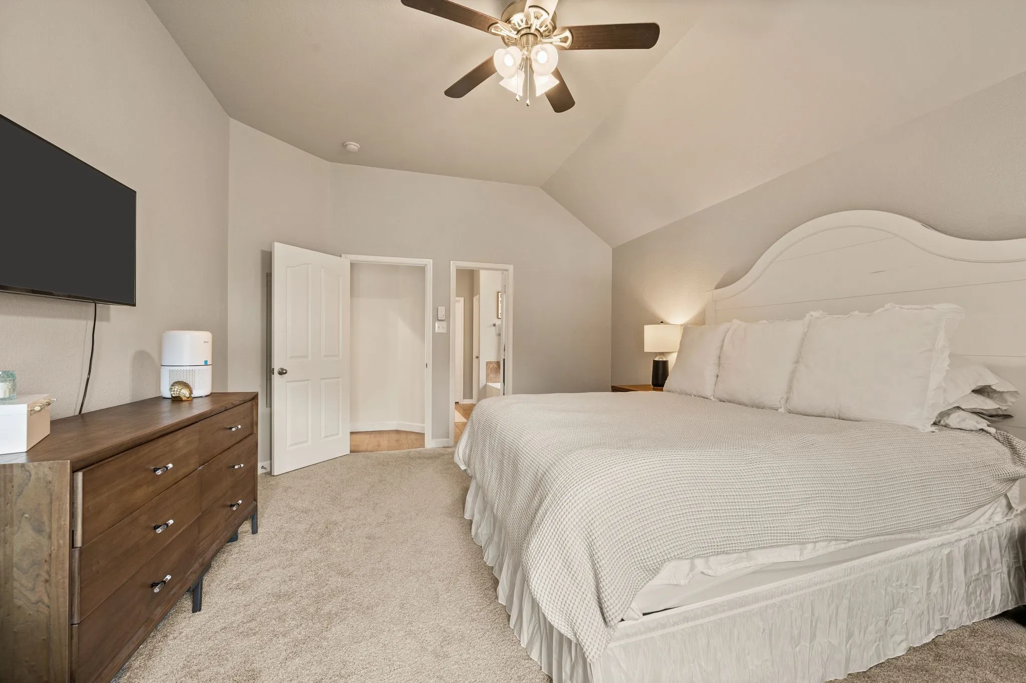 Vaulted ceiling, ceiling fan with light fixture, light gray wall paint, light-colored carpet flooring, white paneled interior door