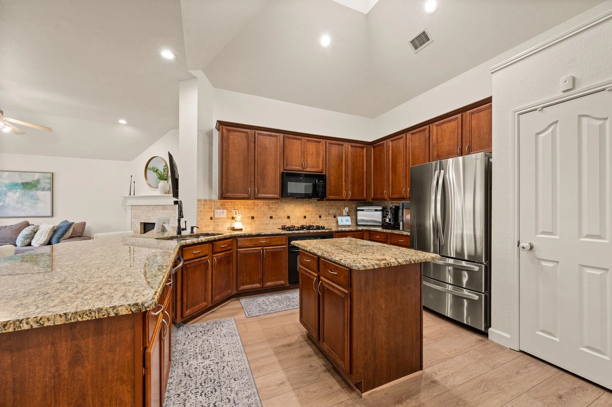 Kitchen featuring wood-finish flooring, granite countertops, wood cabinetry, a stainless steel refrigerator, and recessed lighting