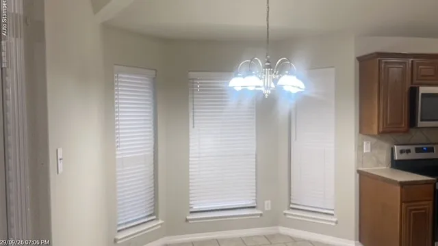 Bay window with three windows, a ceiling-mounted chandelier, tile flooring, wood-finish cabinetry, and stainless-steel appliances