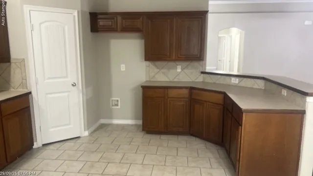 Wood-finish cabinetry, tile flooring, tile backsplash, and a multi-level countertop