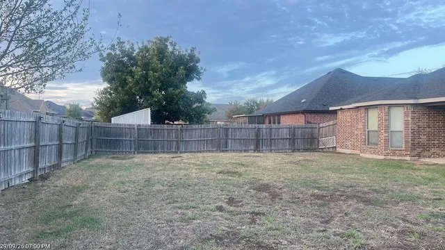 Fenced backyard with a brick exterior, shingled roof, and mature trees