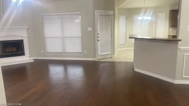 Hardwood-finish flooring, a white mantel fireplace, a large window with blinds, a built-in breakfast bar, and vaulted ceilings